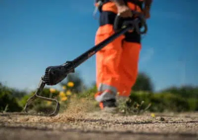 photographie d'une bineuse électrique en action, on peu voir la terre qui vole. l'image montre un détail de cette action d'un homme des espace vert