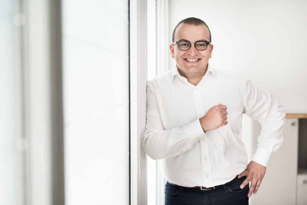 Article Portraits in situ en entreprise par Photo-entreprise-lyon photographies à Lyon bourgoin-jallieu Benoit Gillardeau photographie d'un homme avocat heureux. il est l'épaule contre le mur, il porte des lunettes, l'image est claire