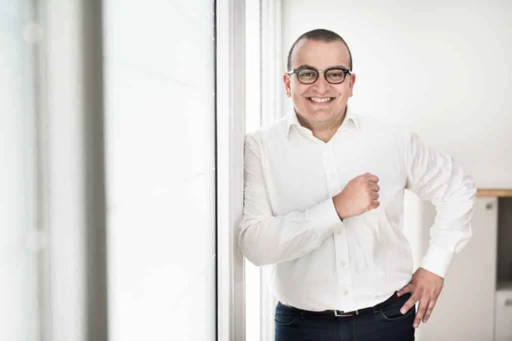 photographie d'un homme avocat heureux. il est l'épaule contre le mur, il porte des lunettes, l'image est claire