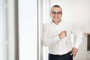 photographie d'un homme avocat heureux. il est l'épaule contre le mur, il porte des lunettes, l'image est claire